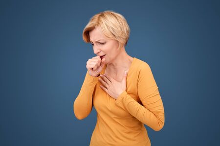 Coronavirus Concept. Blonde woman standing isolated on blue ccoughing wincing from painの写真素材