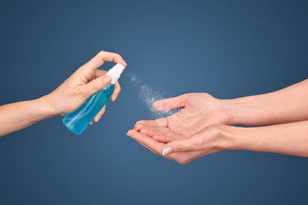 Healthcare protection concept. Cropped view of two woman disinfects palm hands using spray, standing isolated on blue background with copy spaceの写真素材