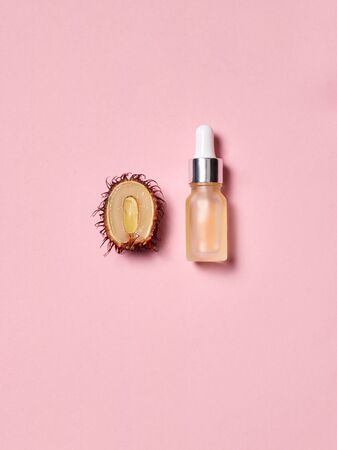 Concept of natural cosmetic or beauty products. Top view of bottle anti aging serum oil with pipette on pastel pink background near rambutan fruitの写真素材