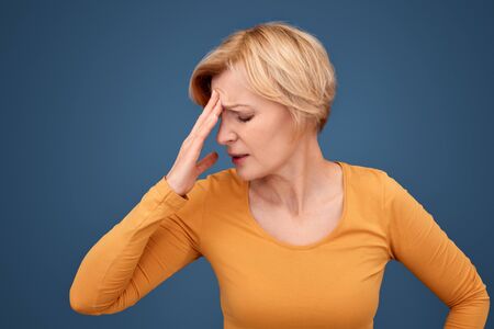 Mature woman holding hand on head, feeling painの写真素材