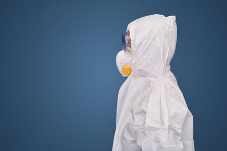 Woman doctor in white hazmat suit standing against blue backgroundの写真素材