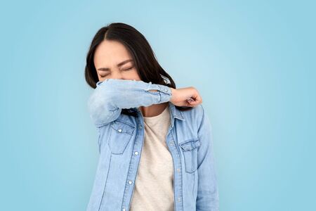 Coronavirus Concept. Chinese woman standing isolated on grey sneezing into jacketの写真素材