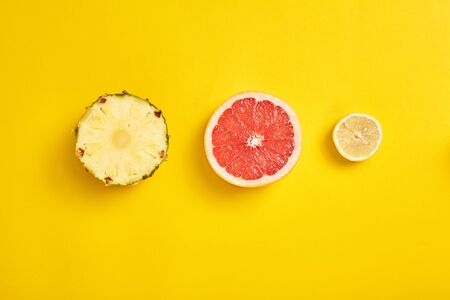 Concept of vitamin food. Top view of sliced tropical pineapple, juicy grapefruit and lemon lying on bright yellow background with copy spaceの写真素材