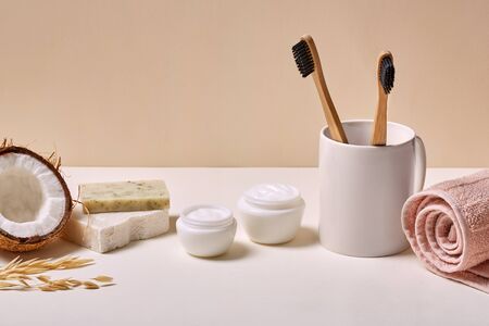 Two eco-friendly bamboo toothbrushes in cup facial cream in jar organic coconut soap and towel isolated in bathroom close-upの写真素材