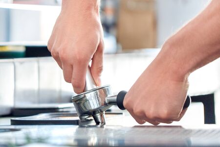 Young man barista standing at coffee shop holding portafilter tamping grounded coffee close-upの写真素材