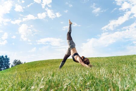 Young woman outdoors on field maintaining healthy lifestyle doing yoga standing on arms leg up balanceの写真素材
