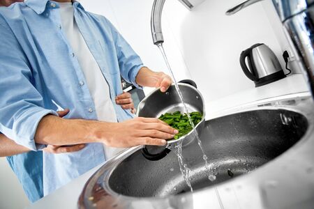 Cropped view of two young adult homosexual guy spending free time at home, standing on kitchen together, hugging, washing ingredients for cooking healthy foodの写真素材