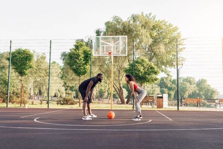 Outdoors Activity. African couple standing on centercourt ready to start basketball game looking at...