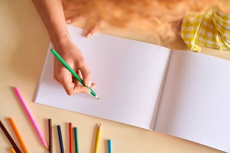 Young woman sitting at table at home drawing using color pencils spending weekend art therapy top view close-upの写真素材
