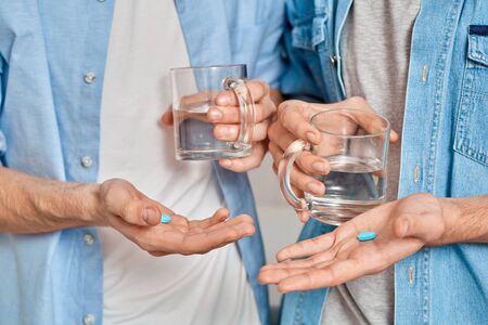 Cropped view of gay couple holding mug with water and pre exposure HIV protection pills in hands, care about health and wellnessの写真素材