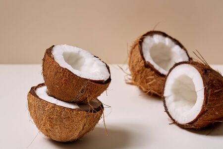 Concept of natural and healthy products. Selective focus of few broken shell or half coconut lying on white beige backgroundの写真素材
