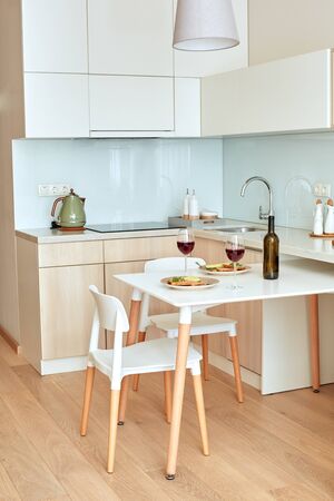 Modern beautiful kitchen sweet interior in daylight no people weekend lunch on the table red wine in glasses and toasts on plateの写真素材