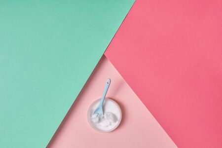 Glass jar of coconut cream with spoon isolated on pink and turquoise background beauty careの写真素材