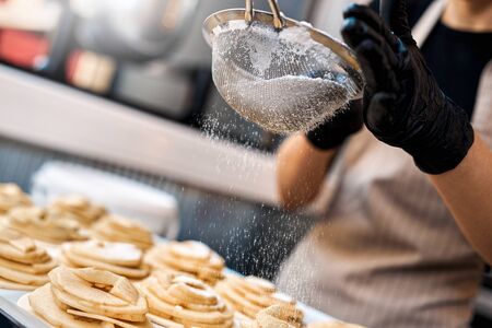 Cropped view of young adult female working on kitchen in bakery store, making delicious dessert on homemade recipe, sprinkled buns with sugar powderの写真素材