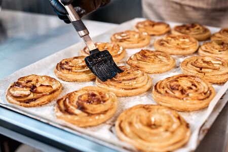 Cropped view of professional chef in gloves working on kitchen in bakery manufacturing, cooking fancy bread, using brush and applying oil on pastryの写真素材