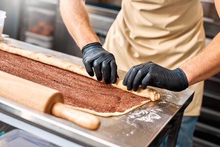 Cropped view of professional chef working in gloves, standing on kitchen in commercial bakery, cooking fancy bread, making sweet cinnamon rollsの写真素材