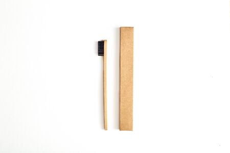 Concept of choosing natural products. Flat lay of paper case and ecological bamboo toothbrush with black nylon bristles on white backgroundの写真素材