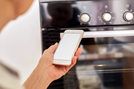Cropped view of pensioner woman standing in kitchen at home, using modern smartphone, holding digital device with copy space on displayの写真素材