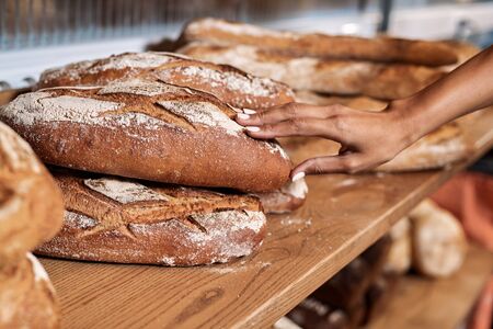 Cropped view of young adult female working in commercial bakery, standing near fresh bread and checking quality of productの写真素材