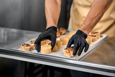 Small Business. Man standing at bakery shop arranging cinnamon rolls on tray close-up