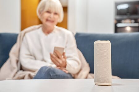 Retirement woman sitting near smart speaker and wireless digital assistantの写真素材