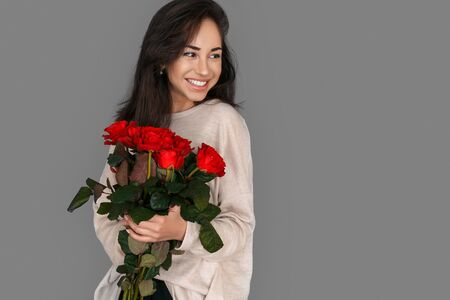 Romantic Present. Woman standing isolated on grey with roses bouquet looking aside joyfulの写真素材