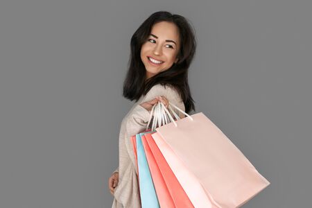Shopping Concept. Woman standing isolated on grey with bags looking aside cheerfulの写真素材