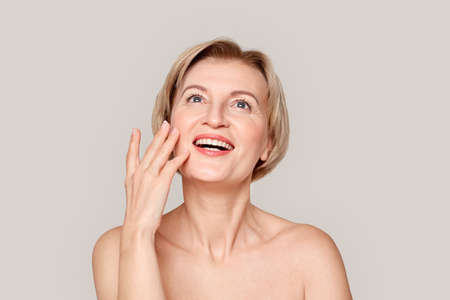 Middle aged model touching her face, looking up with wide smileの写真素材