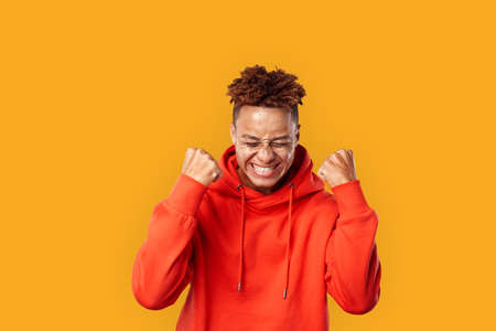Freestyle. Mulatto freckled guy in hoodie standing isolated on yellow hands in fists shouting...
