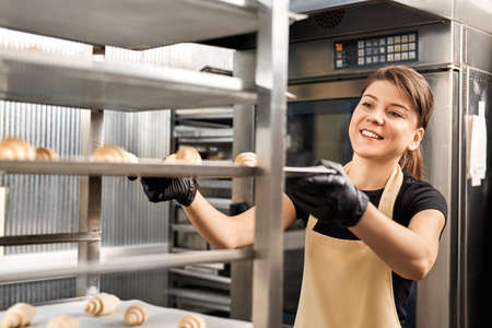 Small Business. Young woman in apron and gloves holding tray of croissants smiling excitedの写真素材
