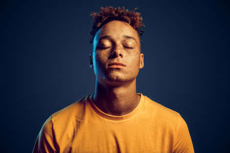 Young adult guy with closed eyes standing against red backgroundの写真素材