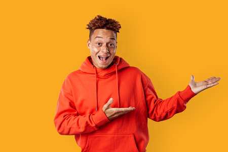 Freestyle. Mulatto freckled guy in hoodie standing isolated on yellow showing copy space smiling excitedの写真素材