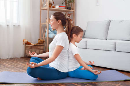 Healthy Lifestyle. Mother and daughter in sportswear doing yoga sitting back to back on mat hands in prayer mediating together smiling peacefulの写真素材
