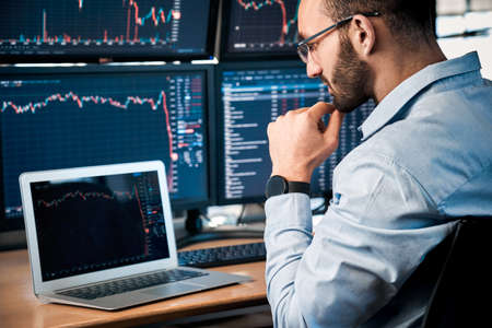 Stock Traiding. Trader sitting at office looking at laptop interpreting candlestick price chart pensive close-upの写真素材