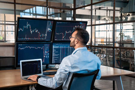 Stock Traiding. Trader sitting at office analyzing price flow on digital screen browsing laptop...