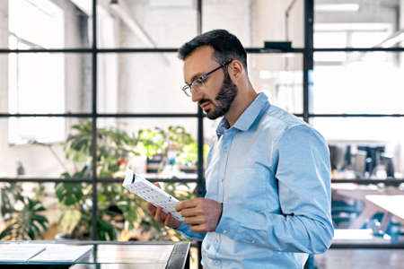 Businessman reading document and standing in officeの写真素材