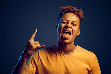 Young adult man showing tongue out and rock n roll signの写真素材