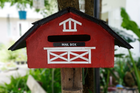 Red handmade mailbox hang on tree in front of house.