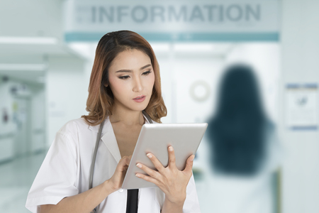 Female doctor working with computer tablet with blue background of hospital front desk information. の写真素材