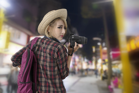 Tourist girl holding camera in hand while walking along with the colorful neon light of Chinese night market.の写真素材