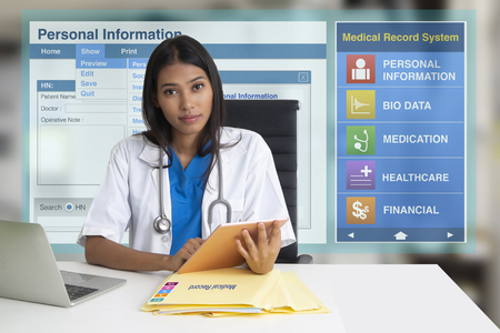 Female doctor sitting in office with electronic medical record screen on background.の写真素材