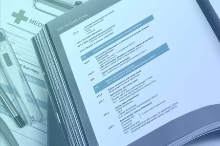 Medical code handbook opens on doctor's desk use for classification of diseases to given code in medical record.の写真素材