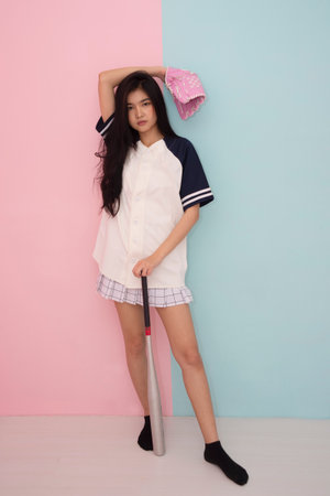 Teenage girl in baseball uniform standing and holding baseball equipment in room.の写真素材