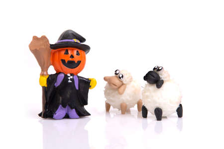 Little ceramic pumpkin witch doll with two sheep on white background for halloween celebration.の写真素材