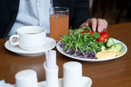 Only one man sits at dining table with healthy breakfast served with orange juice and hot tea.
