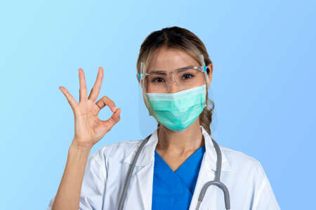 Isolated photo of female doctor in uniform with mask and face shield showing signaling ok.の写真素材
