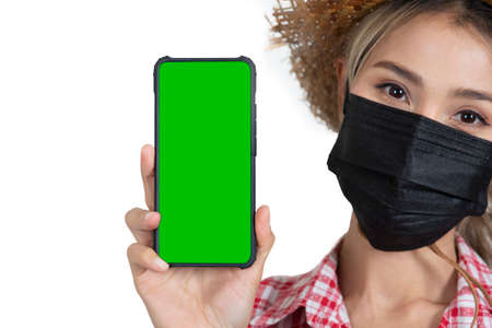 Closed-up female tourist face wareing red plaid shirt with straw hat and face mask holding smartphone shown green sereen on white backgroundの写真素材