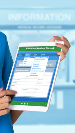Vertical photo of someone hand holding electronic tablet showing blank medical record with blue tone of hospital public relations counter in background.の写真素材