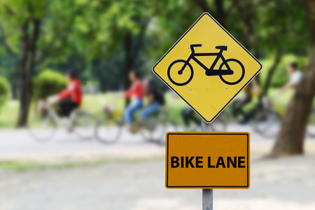 Bicycle lane signs are located in urban green areas where cyclists can be seen moving behind the lane sign.の写真素材