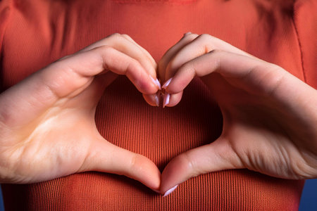 Close-up photo of woman's hands in red sweater making a heart shape symbolizing love on Valentine's Day.の素材